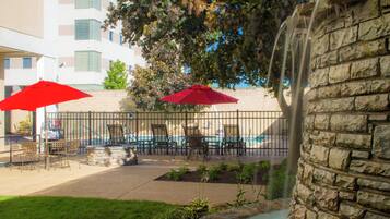 An outdoor patio area with tables and chairs, red umbrellas, and a stone wall.