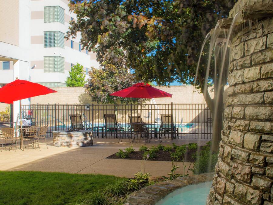 An outdoor patio area with tables and chairs, red umbrellas, and a stone wall.