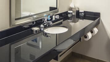 Une salle de bain moderne avec un plan de toilette noir, un lavabo blanc et un grand miroir. On y trouve des serviettes et des articles de toilette sur le plan de toilette.