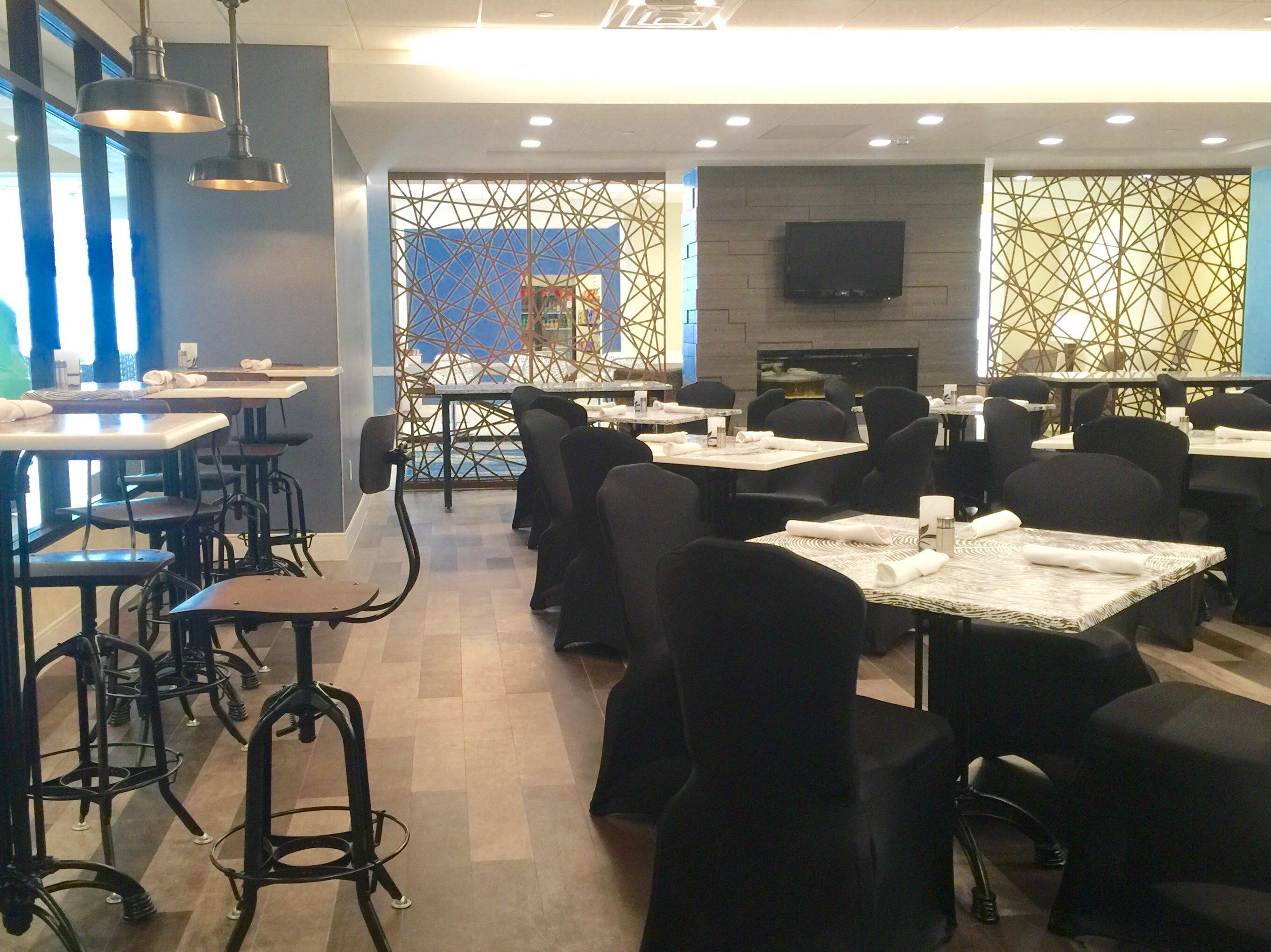 Interior de un restaurante con mesas, sillas y un televisor montado en la pared.