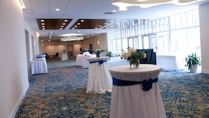 A spacious hall with a patterned carpet, round tables with white tablecloths and blue sashes, and large windows allowing natural light. - Crowne Plaza Suites Pittsburgh South by IHG (Bethel Park)