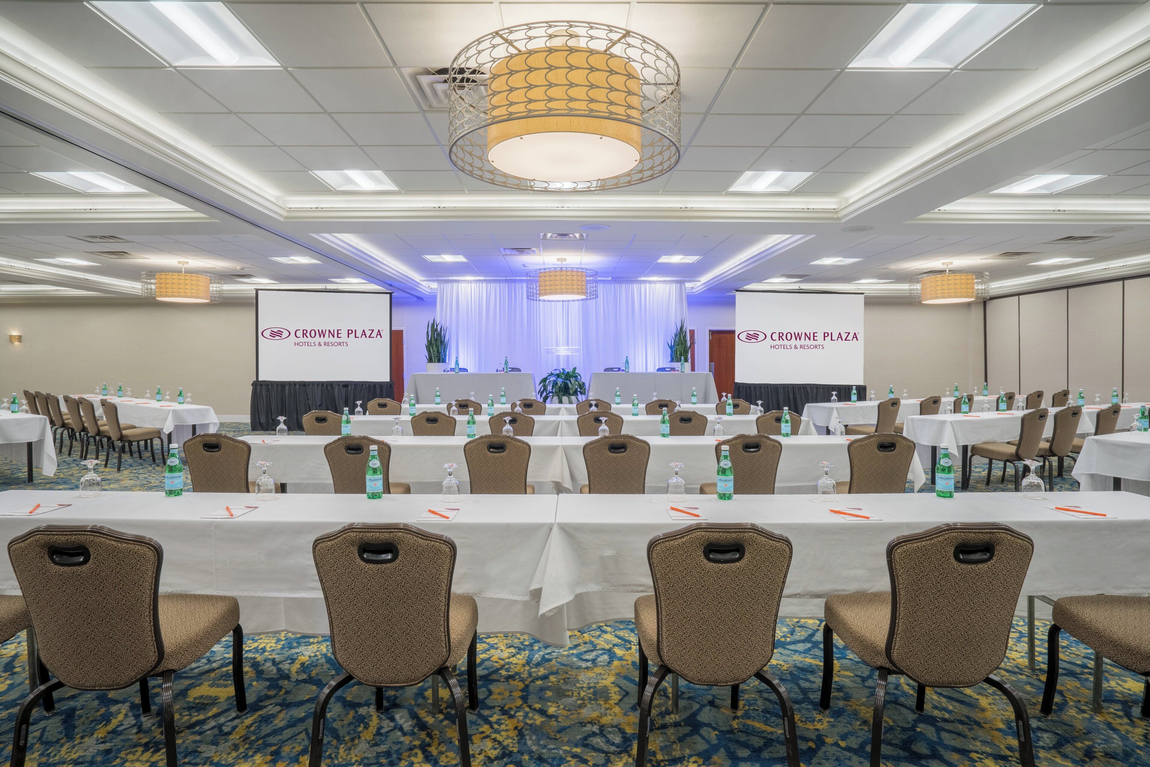 Una sala conferenze con tavoli e sedie, un palco con tende e striscioni per Crowne Plaza Hotels & Resorts.