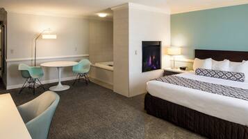 A hotel room with a bed, a desk, two chairs, a TV, and a lamp.