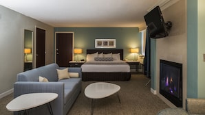A hotel room with a bed, a sofa, a small table, a TV, and a fireplace. - Crowne Plaza Suites Pittsburgh South by IHG (Bethel Park)
