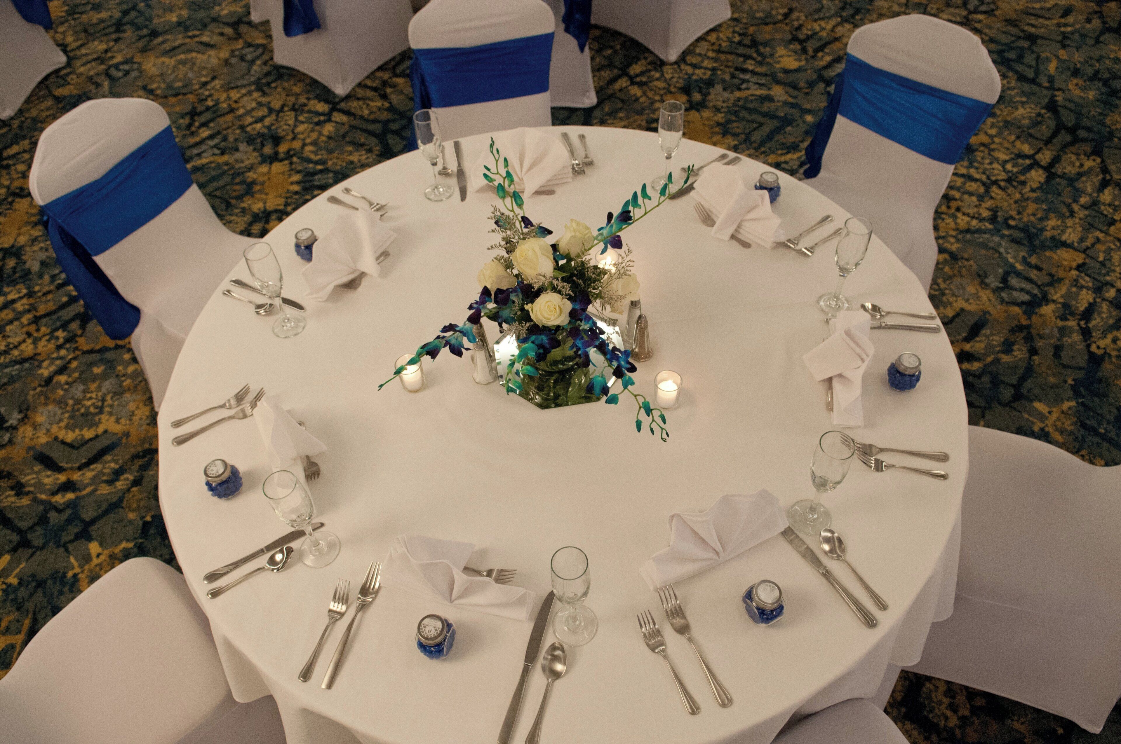 A round dining table with white tablecloth, blue sashes, and a floral centerpiece.