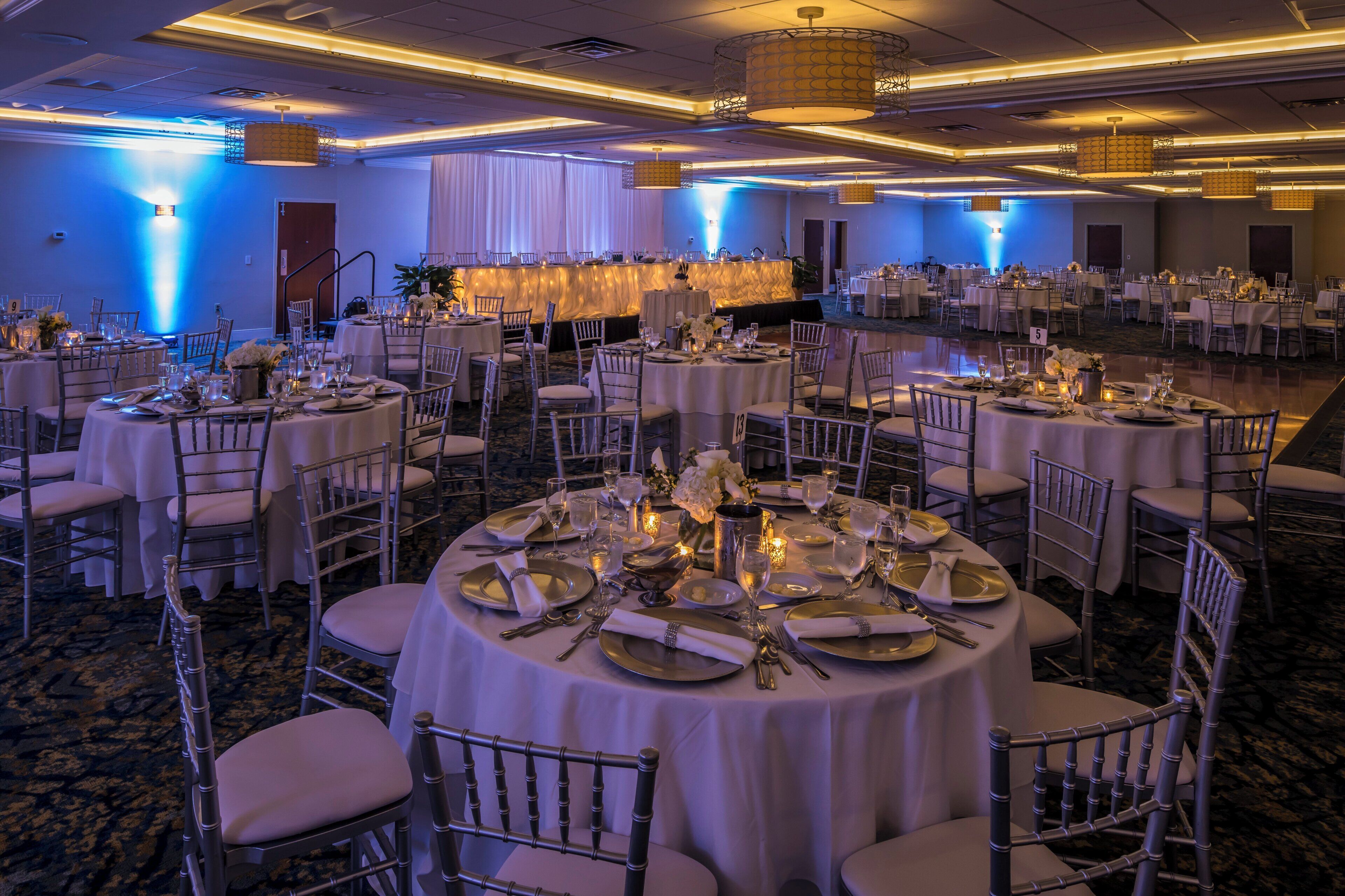 A banquet hall with round tables, chairs, and a stage area.