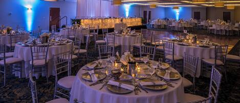 A banquet hall with round tables, chairs, and a stage area.
