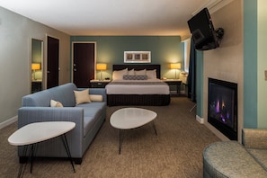 A hotel room with a bed, a sofa, two side tables, a flat-screen TV, and a fireplace. - Crowne Plaza Suites Pittsburgh South by IHG (Bethel Park)