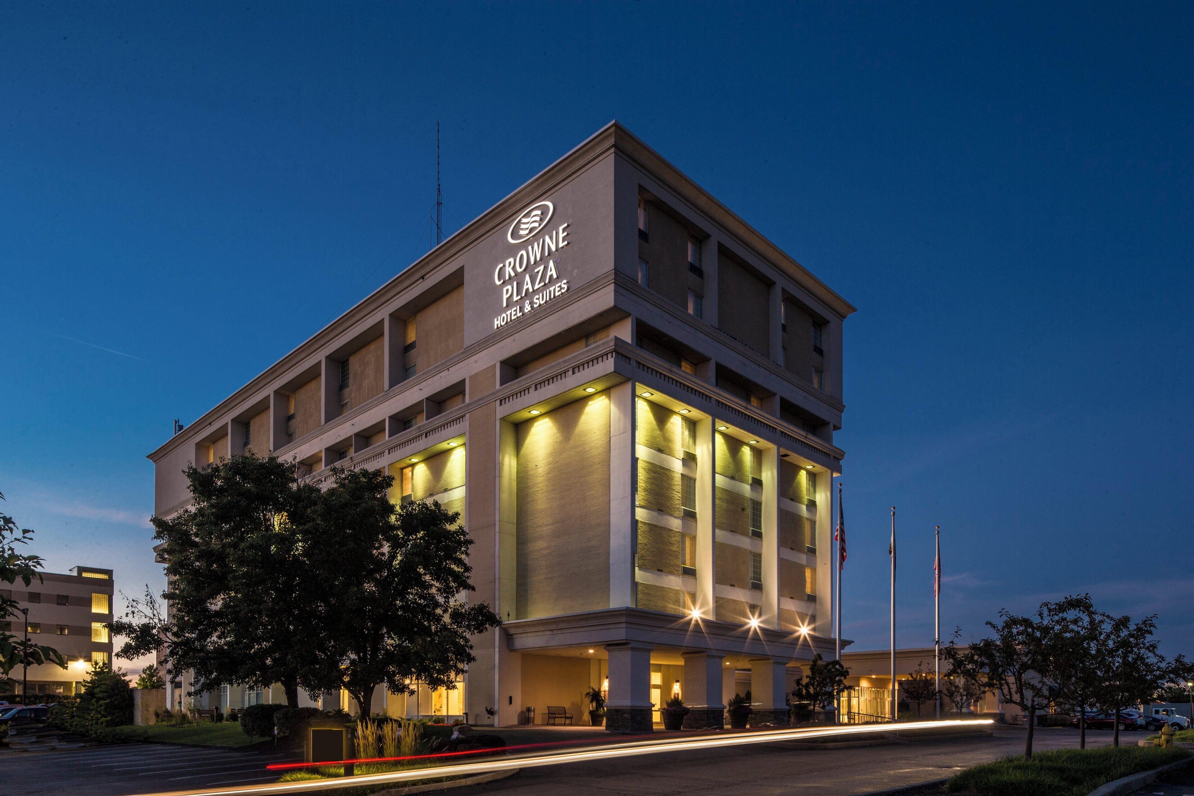 Un immeuble hôtelier à plusieurs étages, avec une enseigne lumineuse indiquant « Crowne Plaza Hotel & Suites ».