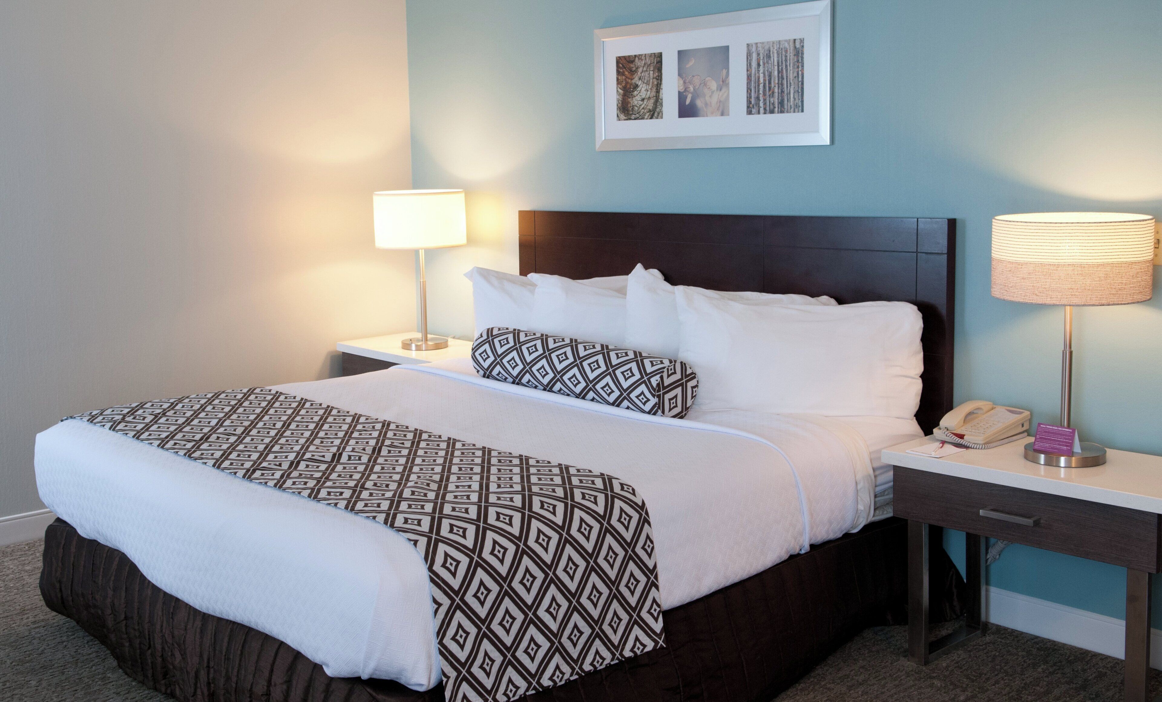 A hotel room with a bed, two bedside tables, a nightstand, a lamp, and a framed picture on the wall.
