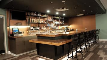 A bar area with a long counter, multiple shelves of bottles, and bar stools.