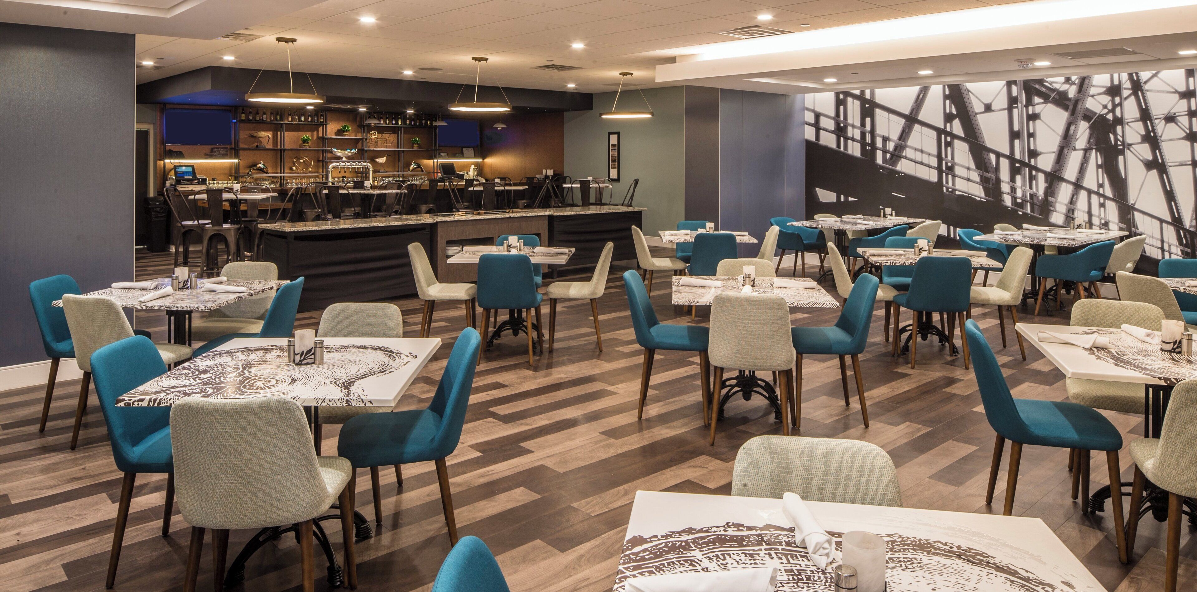 A restaurant with multiple tables and chairs, a bar area, and a large wall mural.