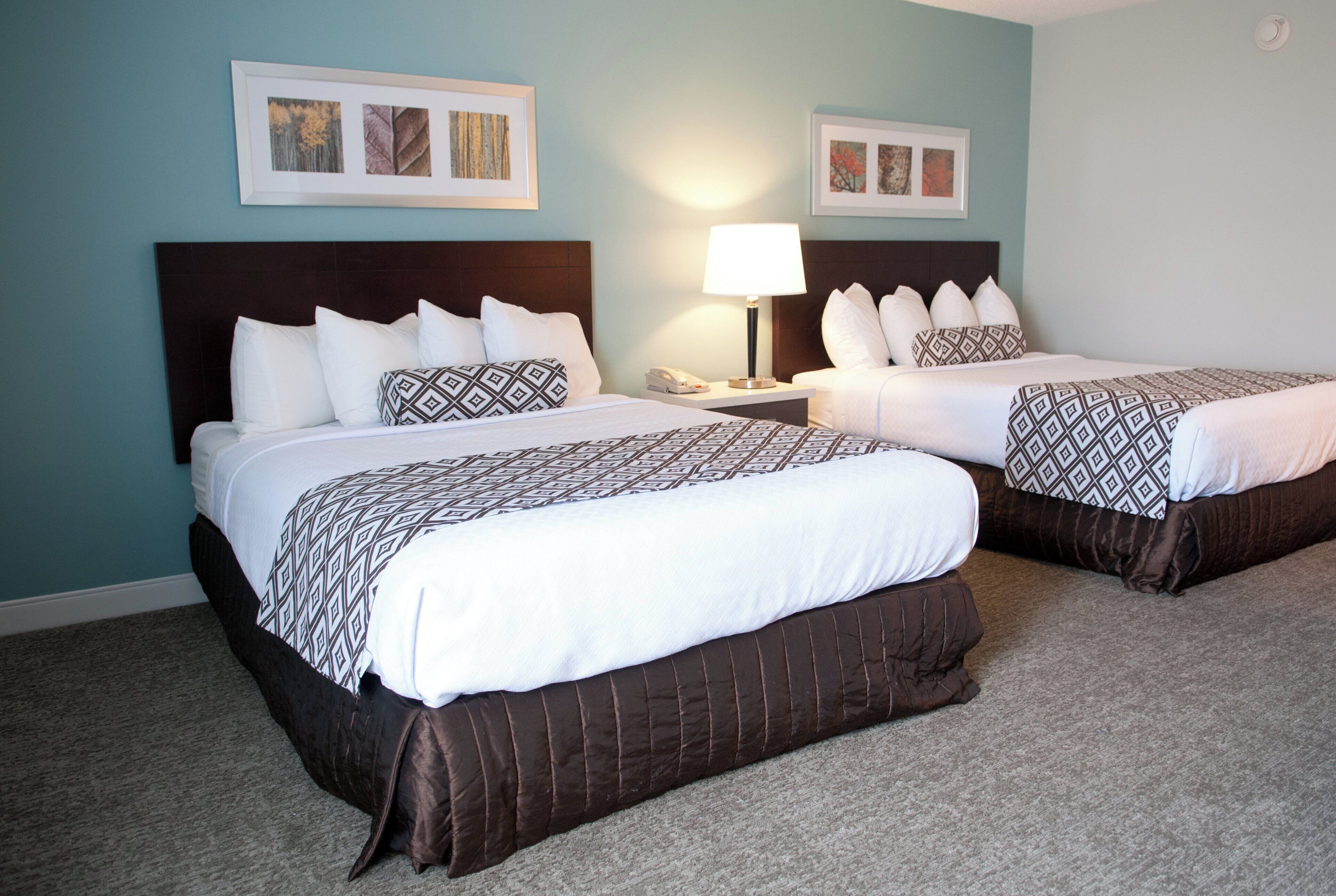 A hotel room with two beds, a nightstand with a lamp, and framed pictures on the wall.