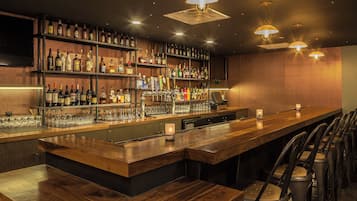 A bar area with shelves of bottles, a cash register, and bar stools.