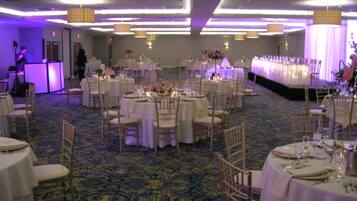 A banquet hall with round tables set for dining, chairs, and a stage area.