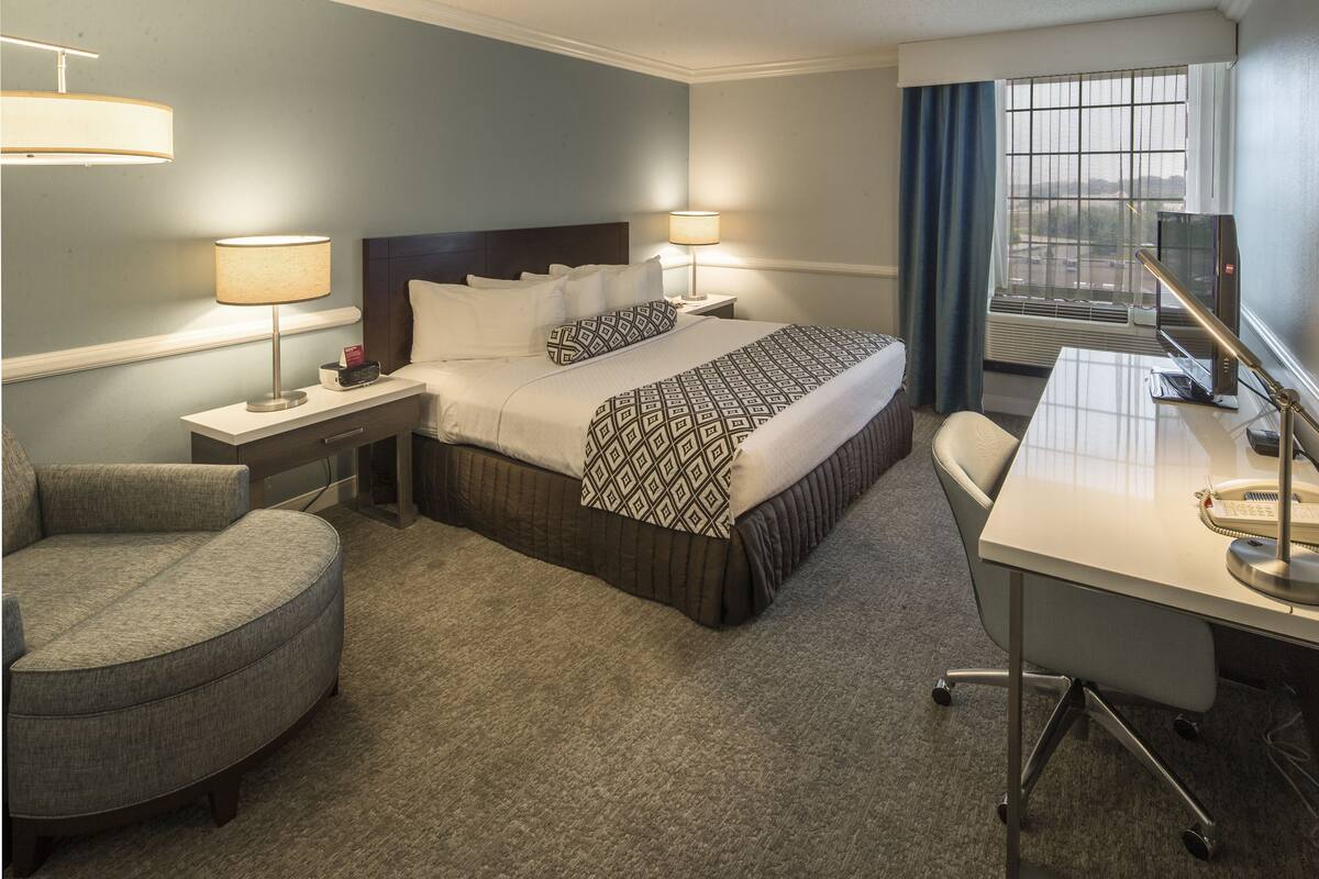 Ein Hotelzimmer mit Bett, zwei Nachttischen, einem Schreibtisch, einem Stuhl und einem Fenster mit Vorhängen.