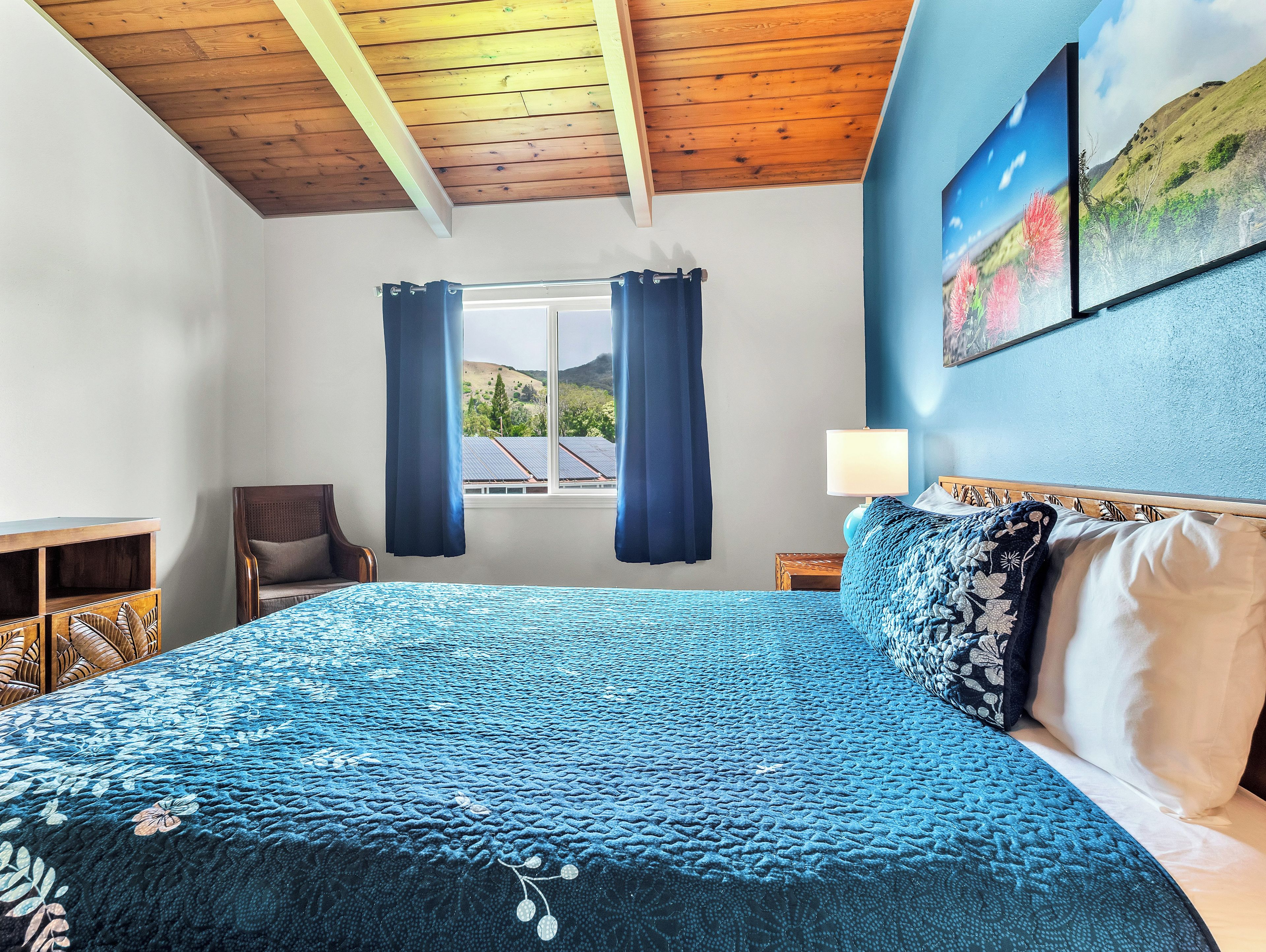 Un dormitorio con una cama grande, una ventana con cortinas, una silla, una mesita y un cuadro en la pared.