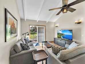 A modern living room with a ceiling fan, a large flat-screen TV, and a view of the outdoors. - Castle Waimea Country Lodge (Kamuela)