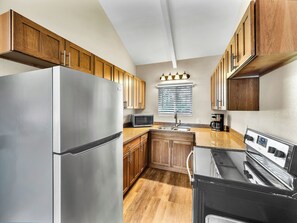 A compact kitchen with wooden cabinets, a stainless steel refrigerator, a microwave, a sink, and a black oven. - Castle Waimea Country Lodge (Kamuela)