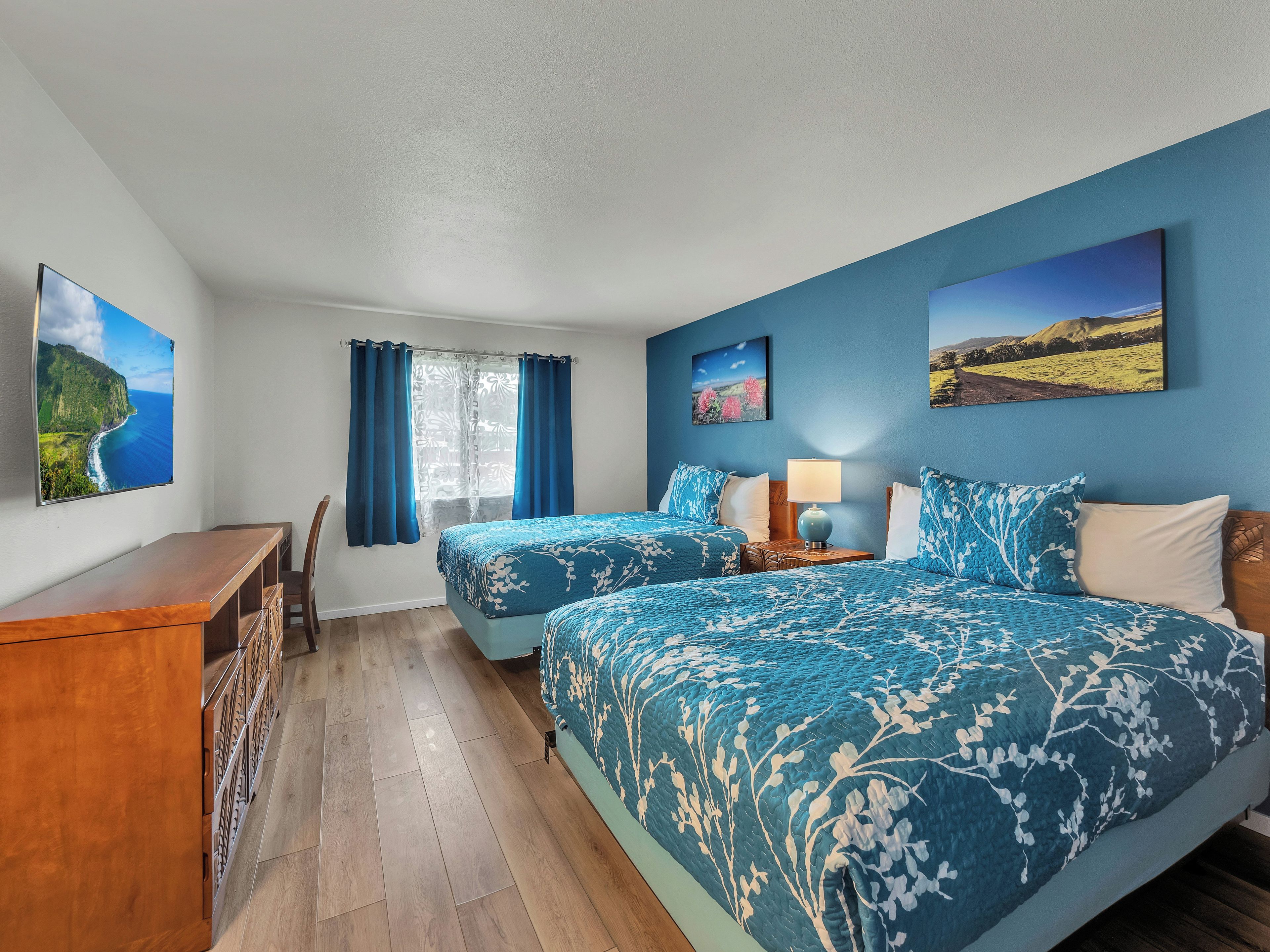 A hotel room with two beds, a desk, and a window with curtains.