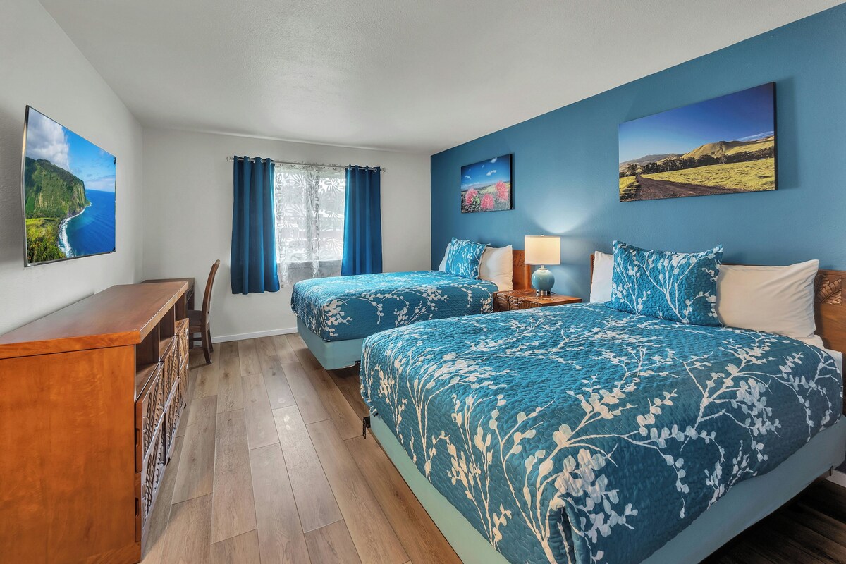 A hotel room with two beds, a desk, and a window with curtains.