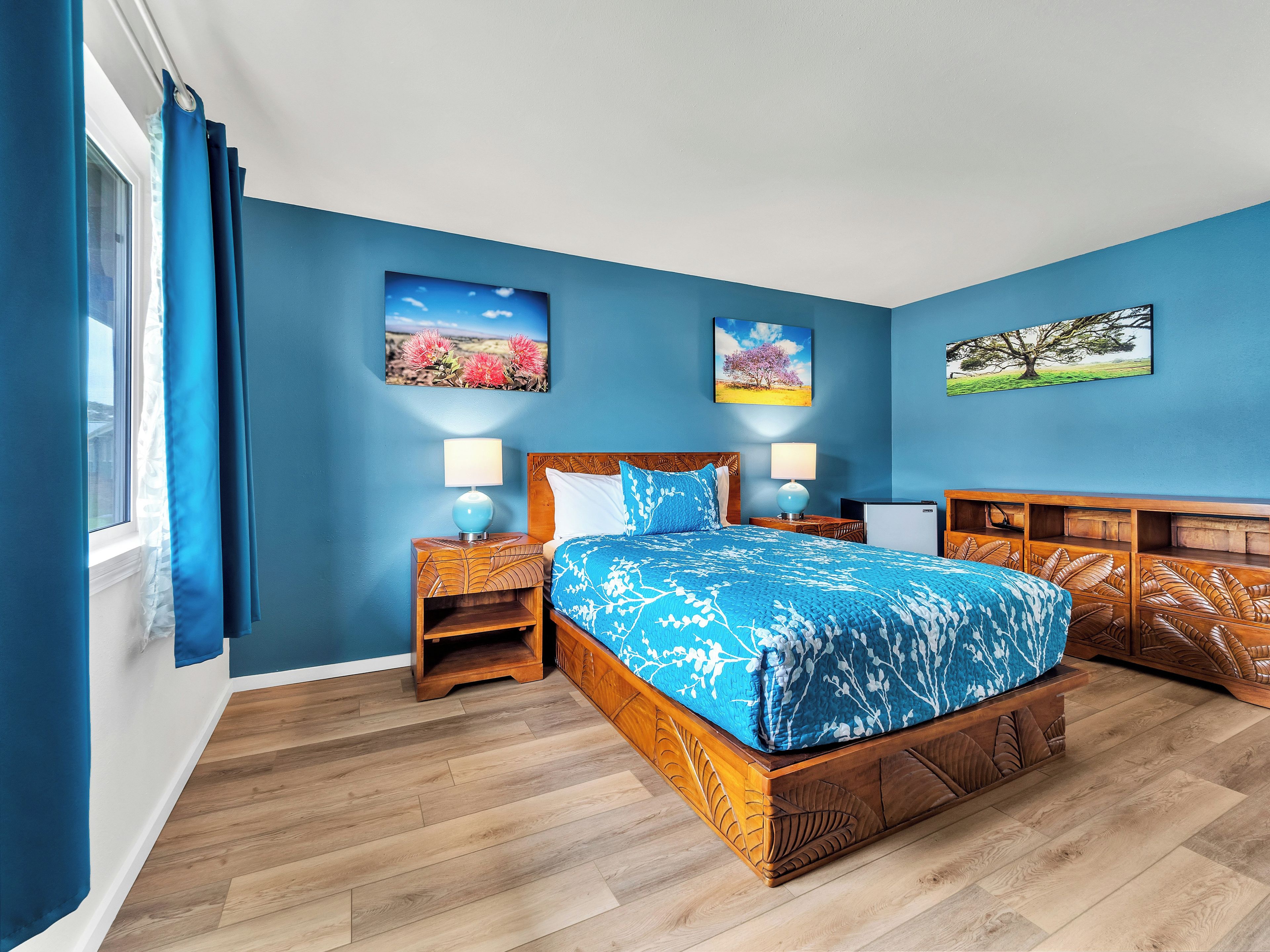 A bedroom with a large bed, two bedside tables with lamps, and three wall-mounted pictures.