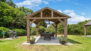A wooden gazebo with a table and chairs, surrounded by grass and potted plants. - Castle Waimea Country Lodge (Kamuela)
