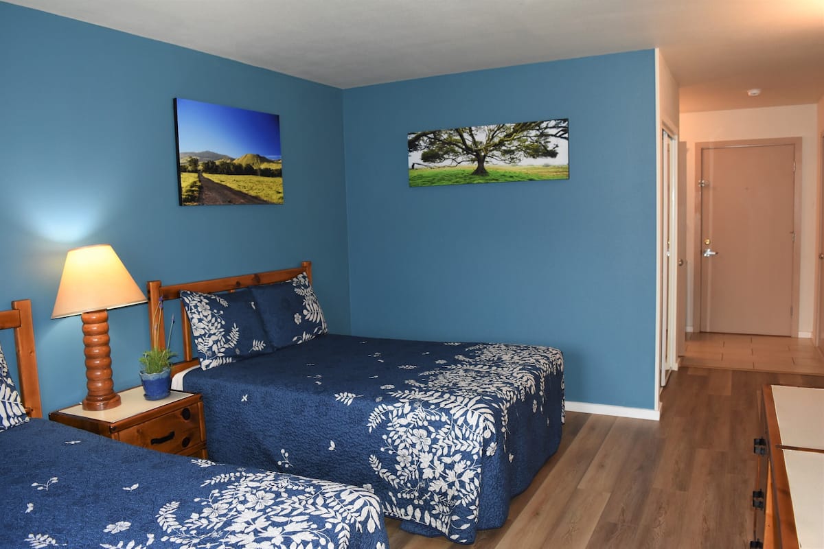 A bedroom with two beds, a nightstand with a lamp, and two wall-mounted pictures.