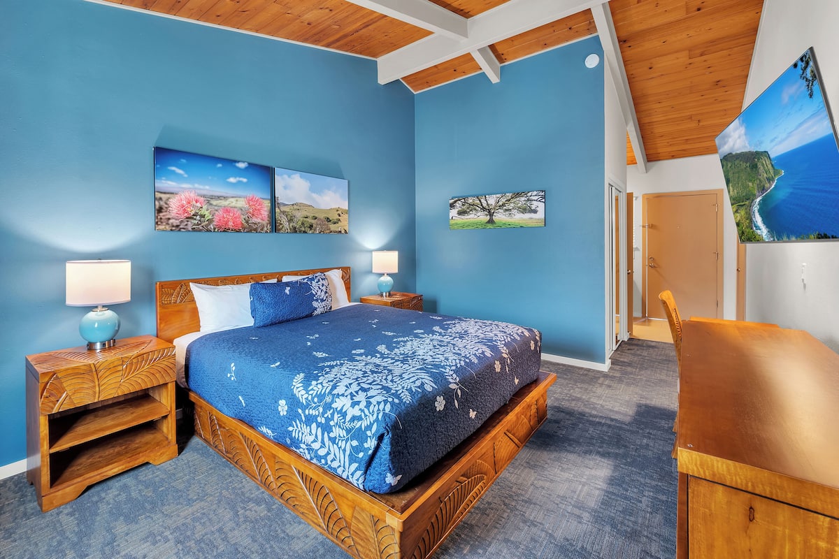 A bedroom with a wooden bed, two bedside tables with lamps, a blue carpet, and three wall-mounted pictures.