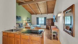 A compact kitchen with wooden cabinets and a central island, a dining area with a wooden table and chairs, and a bedroom with a bed and a wardrobe. - Castle Waimea Country Lodge (Kamuela)
