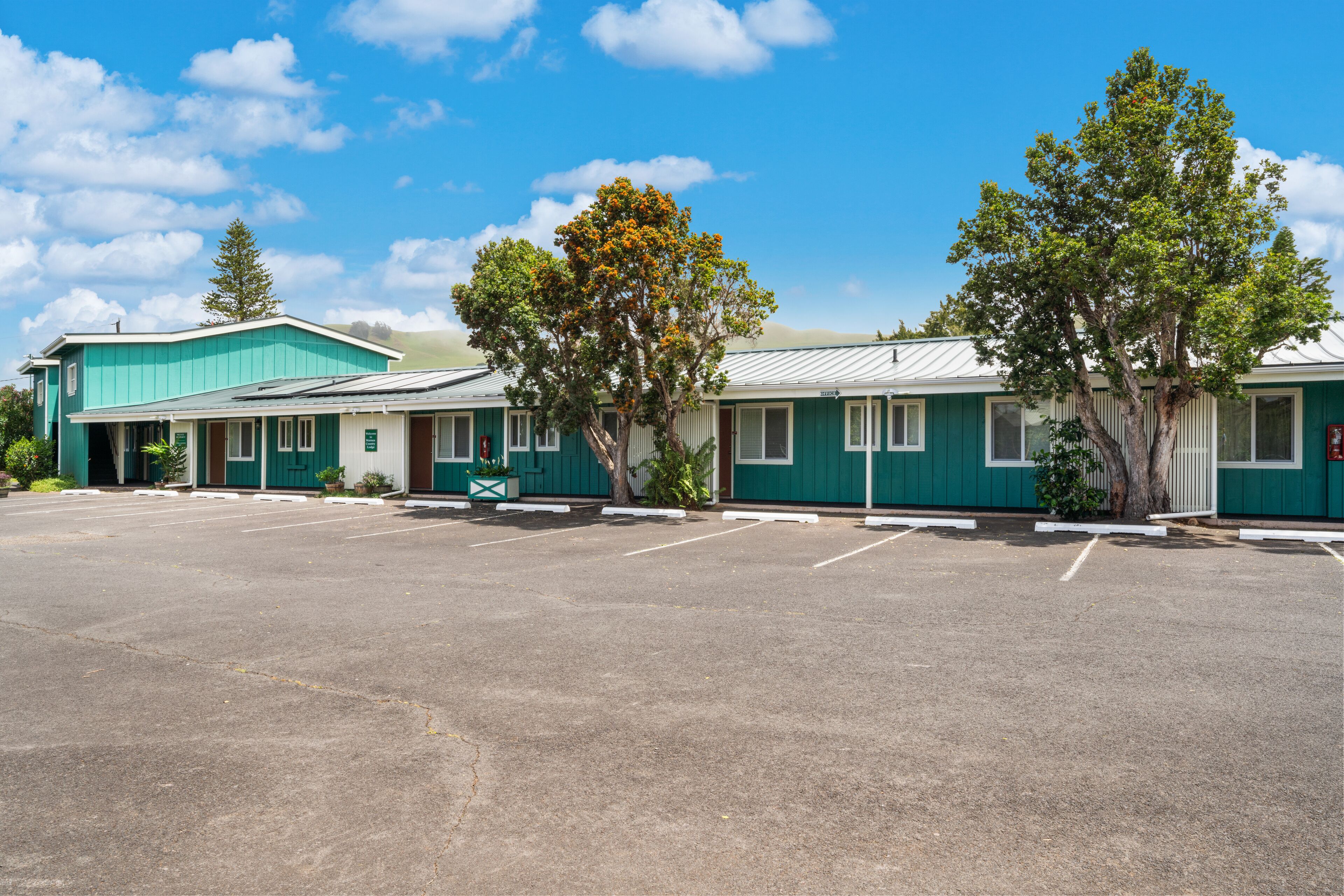 A motel with a parking lot, green exterior, and trees.