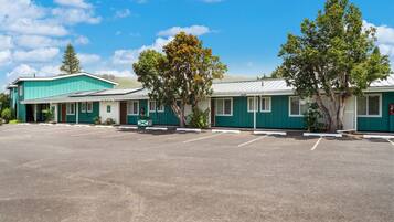 A motel with a parking lot, green exterior, and trees.
