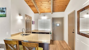 A kitchen with a wooden ceiling, a large island with chairs, and a door with a window. - Castle Waimea Country Lodge (Kamuela)