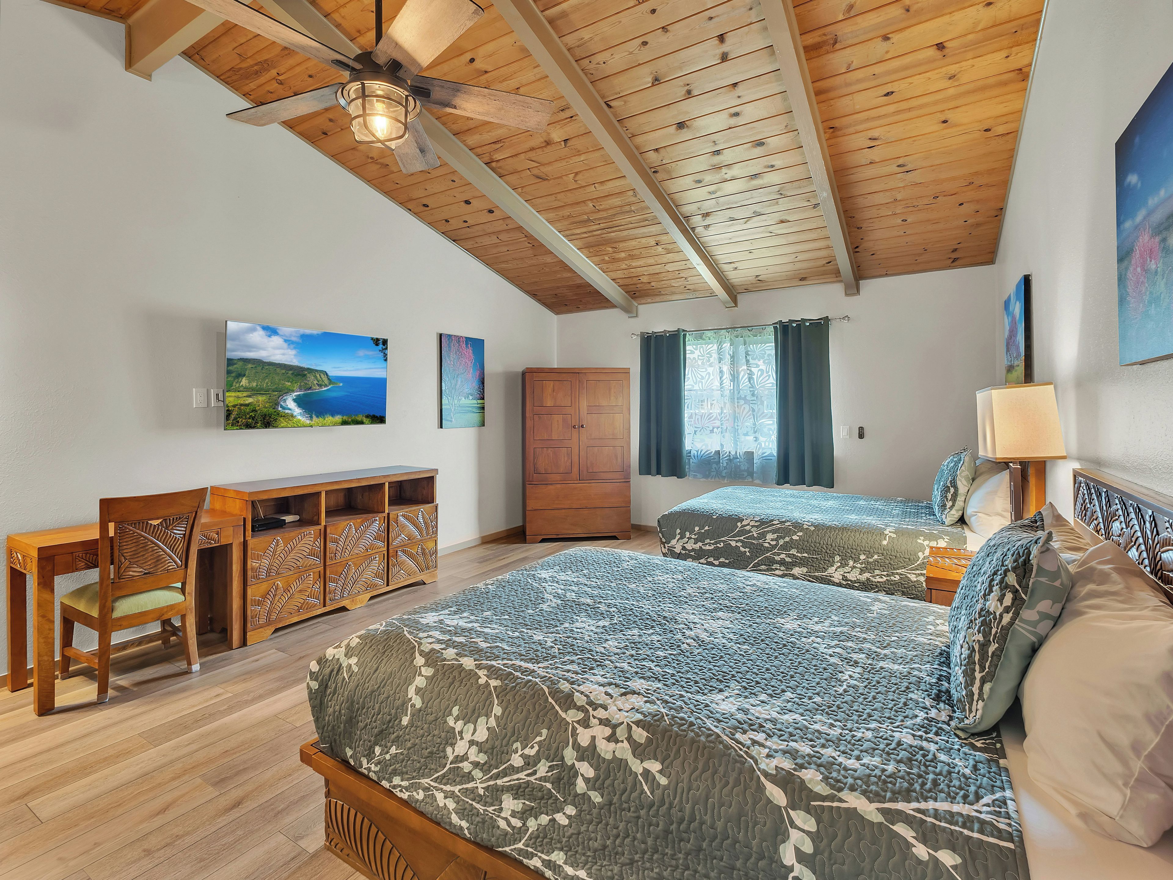 A bedroom with two beds, a wooden ceiling, a TV, and a desk with chairs.
