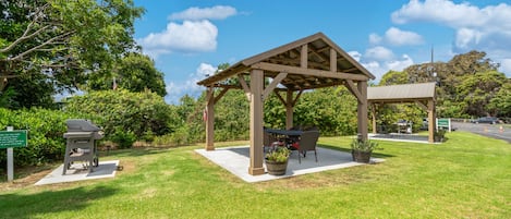 A gazebo with a table and chairs, surrounded by a grassy area and trees.