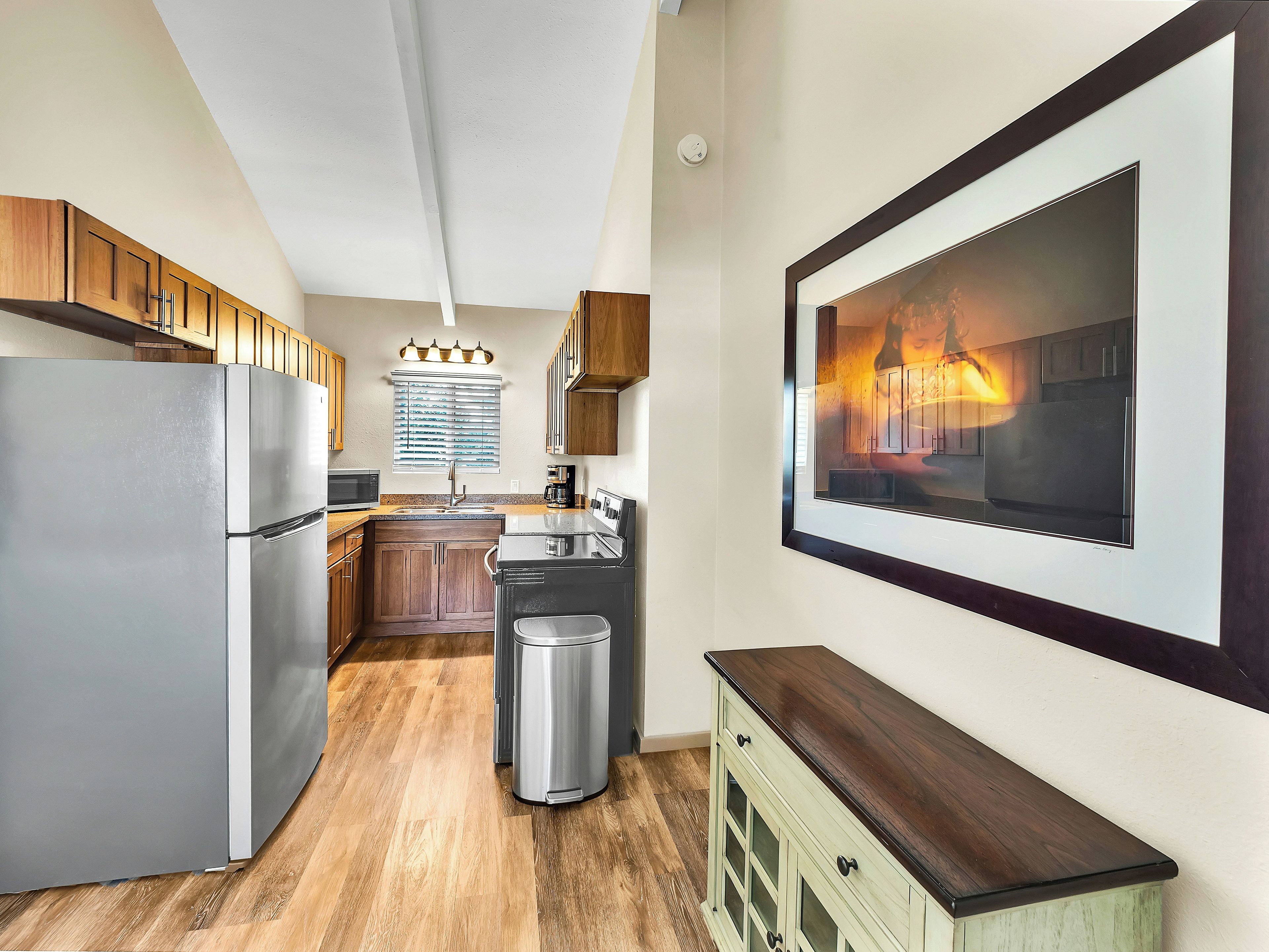Una cocina moderna con refrigerador de acero inoxidable, armarios de madera, pileta de acero inoxidable y un cuadro grande enmarcado en la pared.