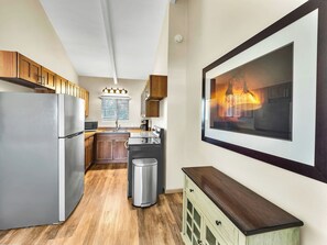 A modern kitchen with a stainless steel refrigerator, wooden cabinets, a stainless steel sink, and a large framed picture on the wall. - Castle Waimea Country Lodge (Kamuela)