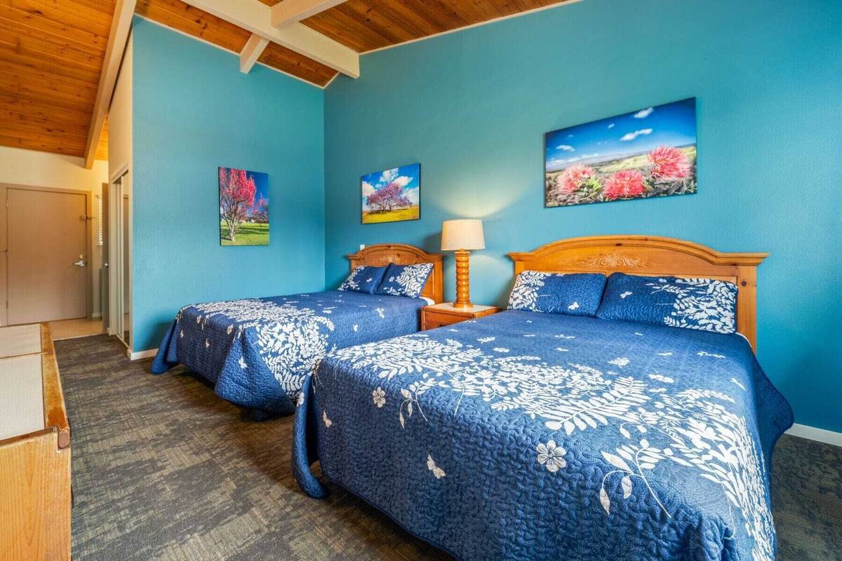 A room with two beds, a wooden ceiling, and three paintings on the wall.