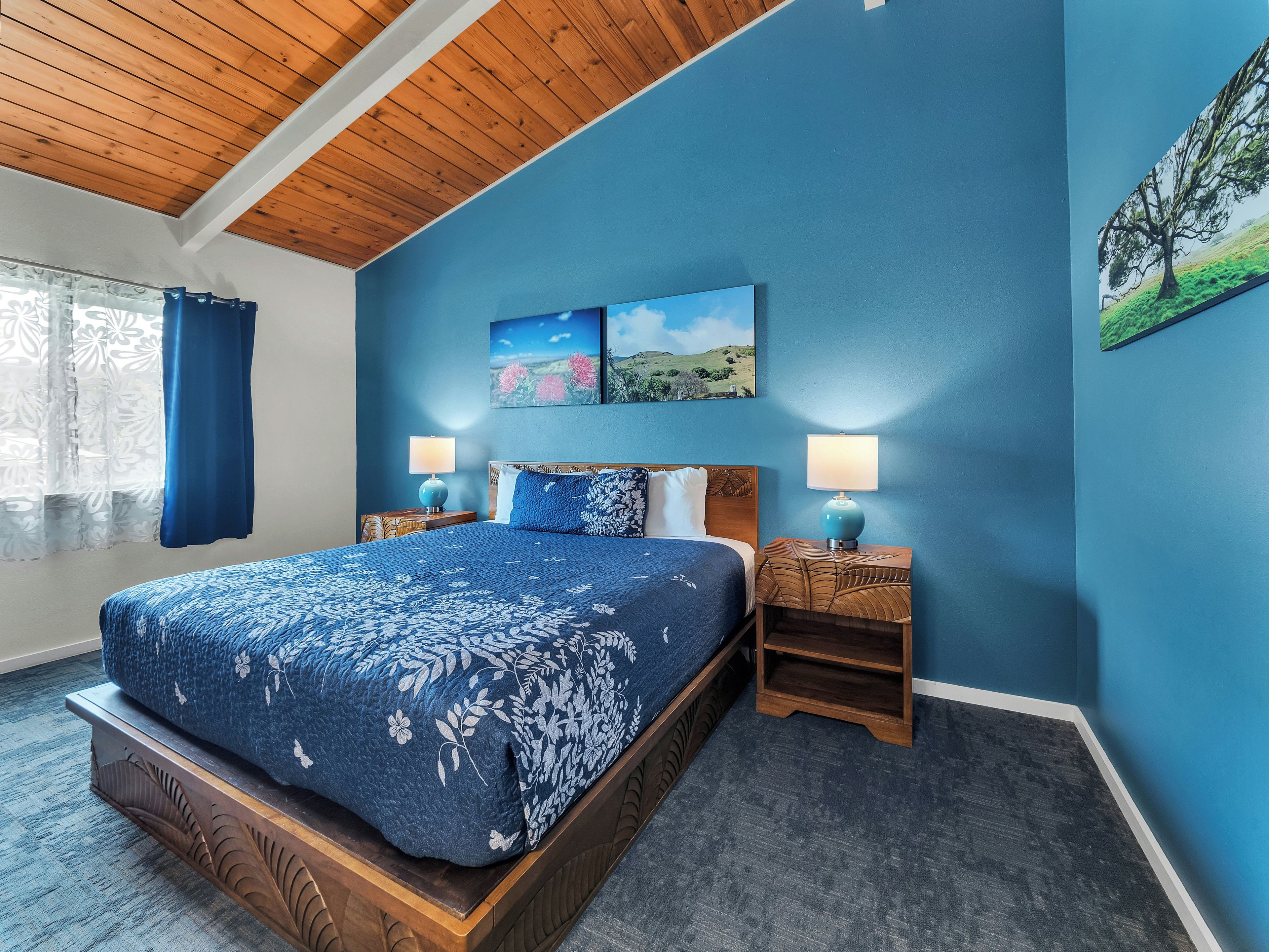 A bedroom with a large bed, two bedside tables, a wooden headboard, and a ceiling with wooden beams.