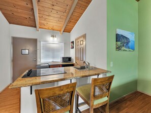A kitchen with a wooden ceiling, a built-in microwave, a sink, and two chairs. - Castle Waimea Country Lodge (Kamuela)