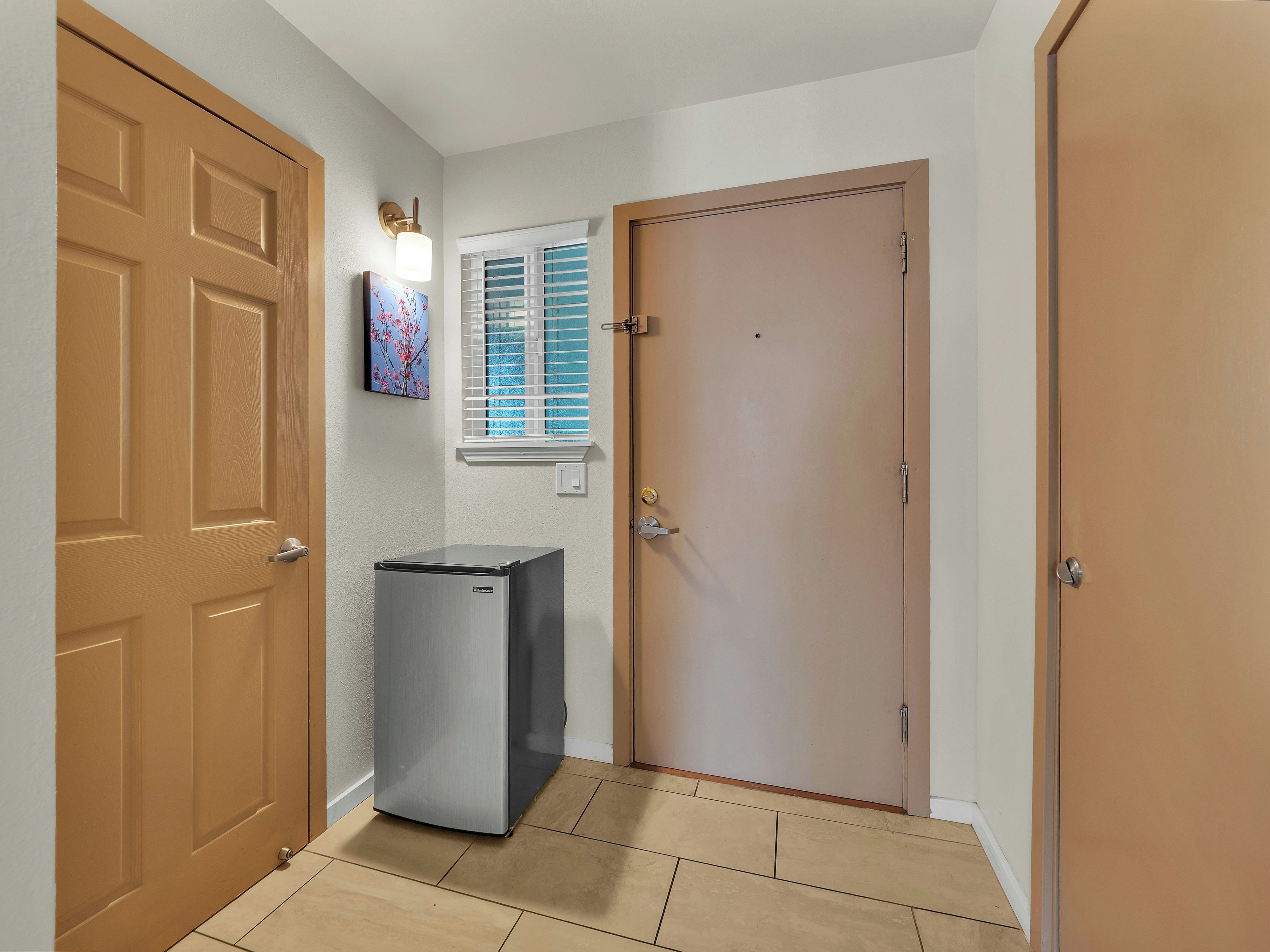 A hallway with a refrigerator, a door, and a window with blinds.