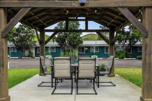 A covered outdoor seating area with a table and chairs, overlooking a parking lot and buildings. - Castle Waimea Country Lodge (Kamuela)