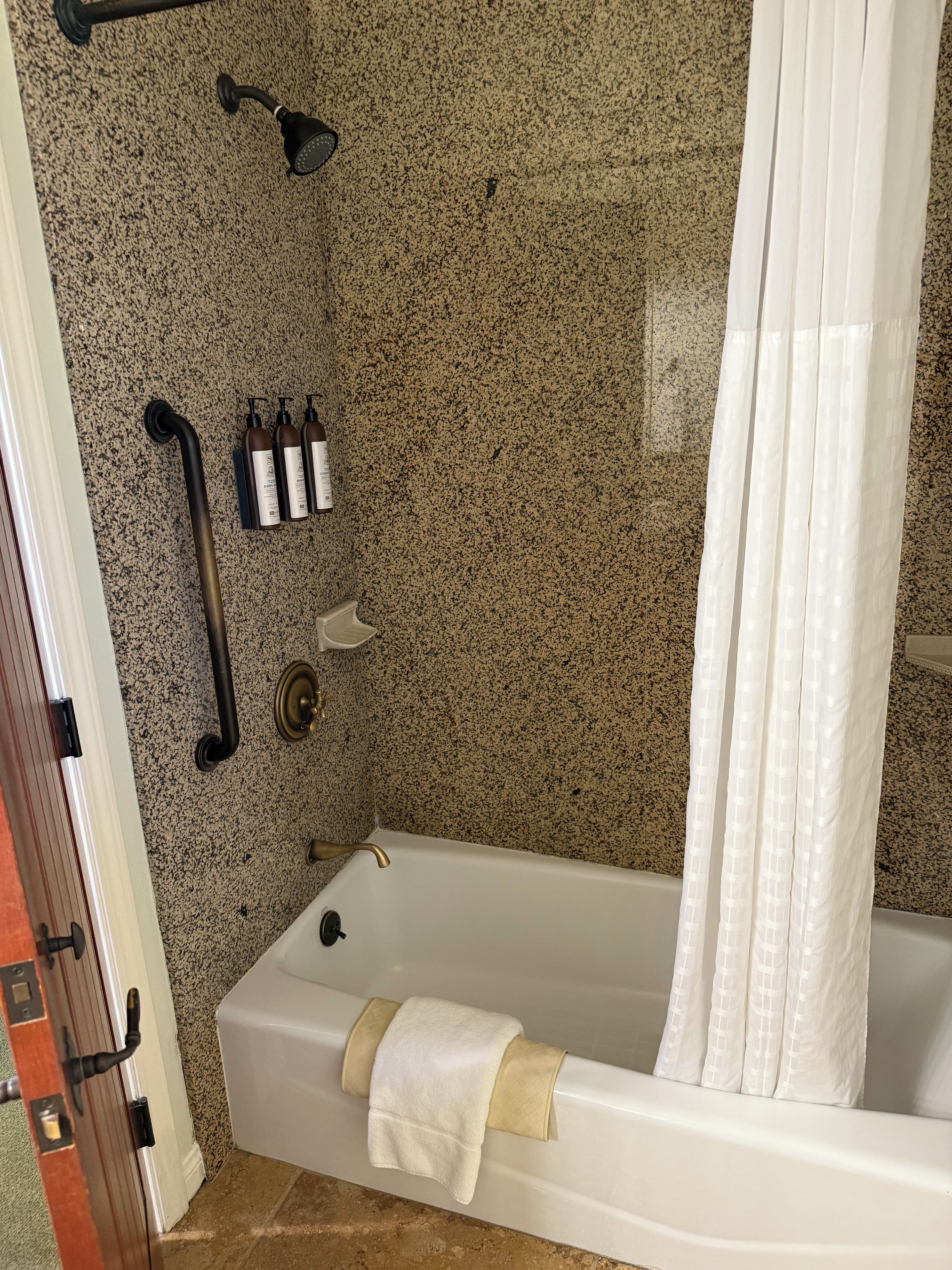 Un baño con bañera, cortina de ducha y toallero con botellas.