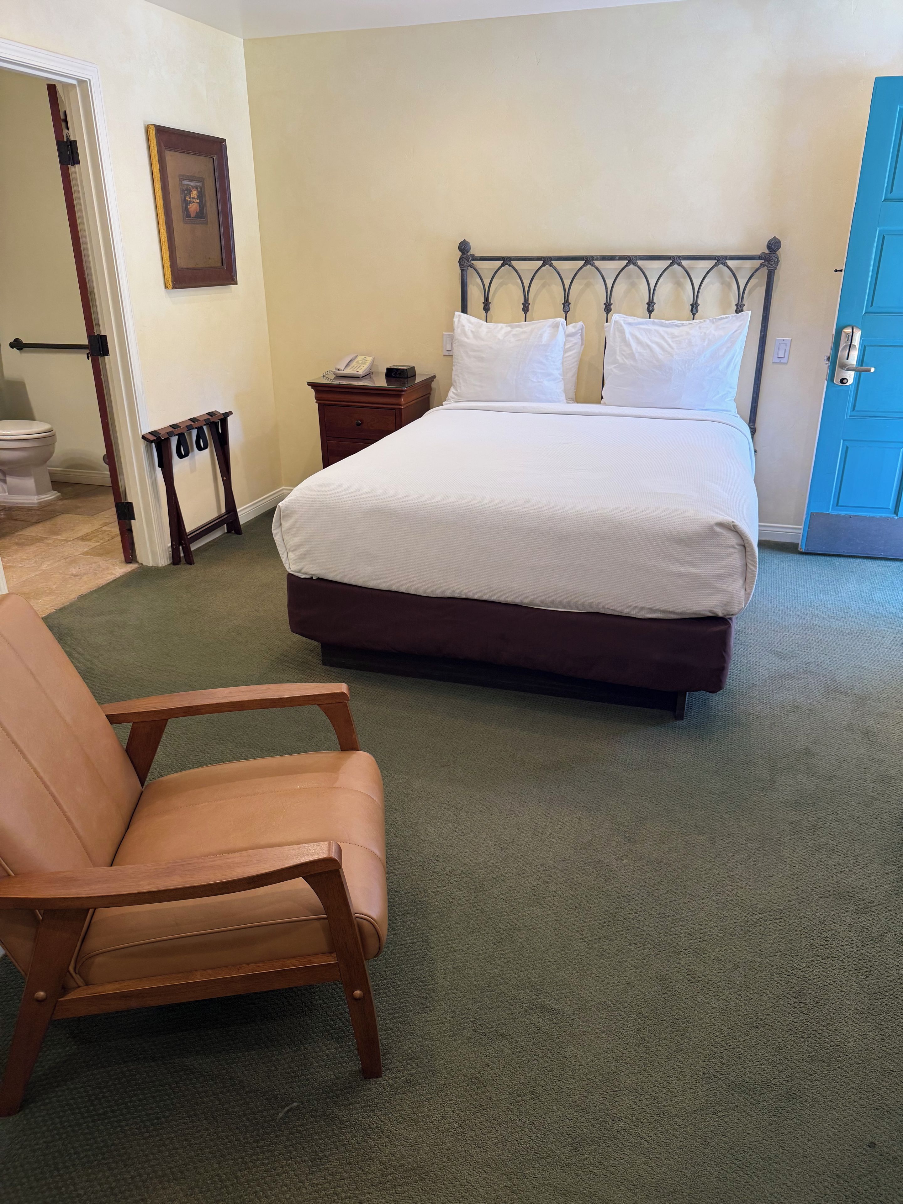 Een hotelkamer met een bed, een stoel, een nachtkastje met een telefoon, en een foto aan de muur.