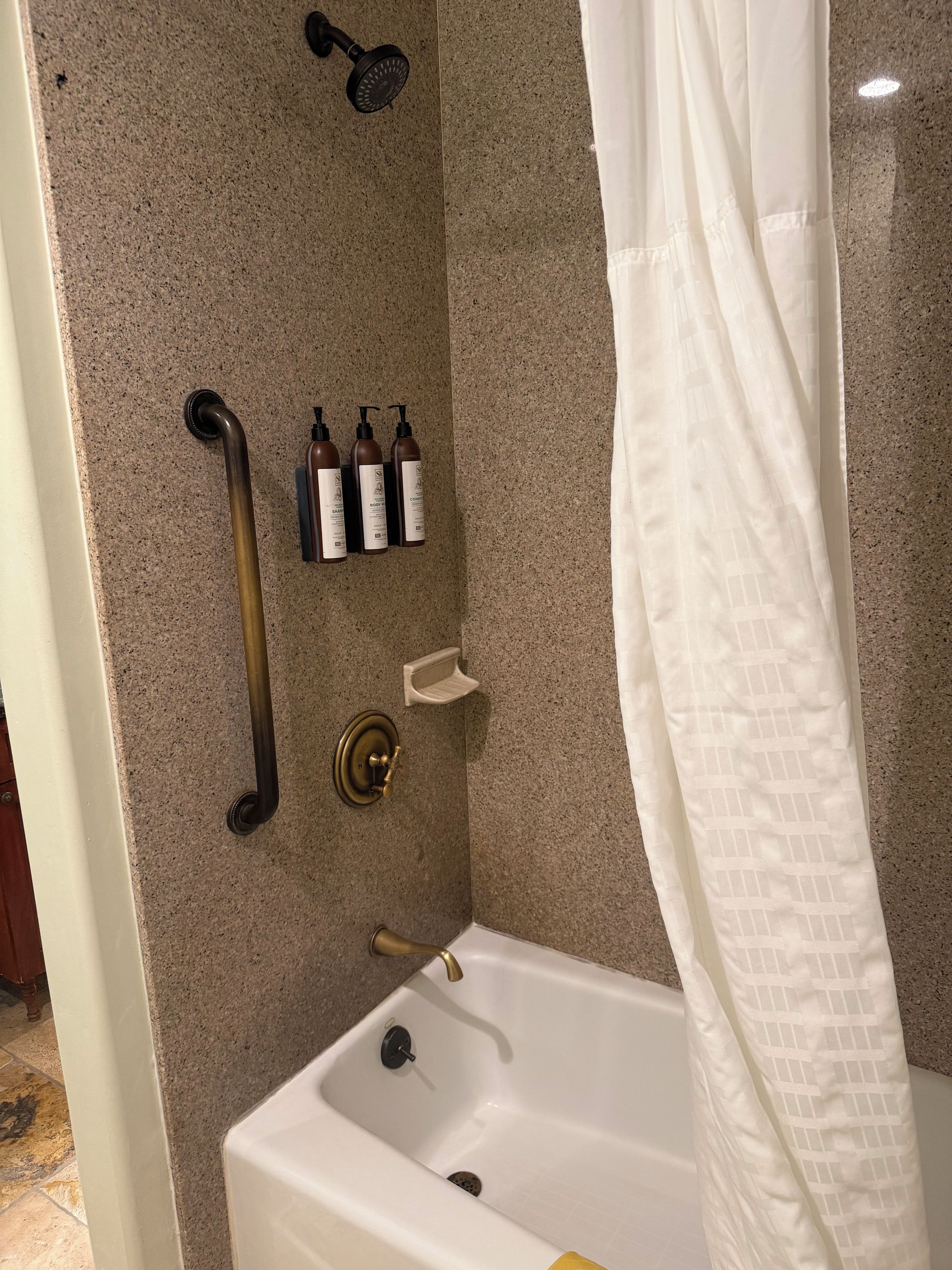 A bathroom with a bathtub, a showerhead, a handrail, and toiletries.