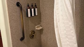 A bathroom with a bathtub, a showerhead, a handrail, and toiletries.