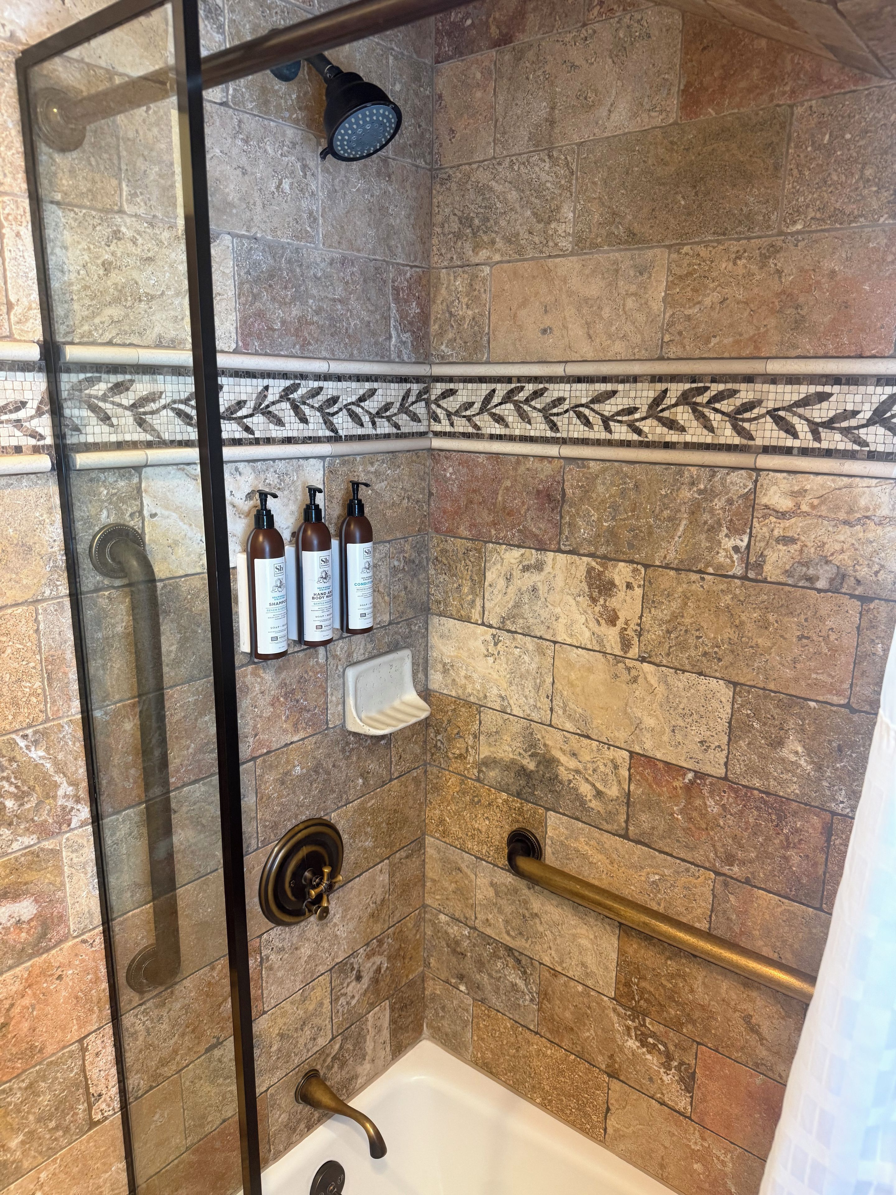 Un espace douche doté d’une porte en verre, d’un pommeau de douche à main et d’un distributeur de savon liquide.