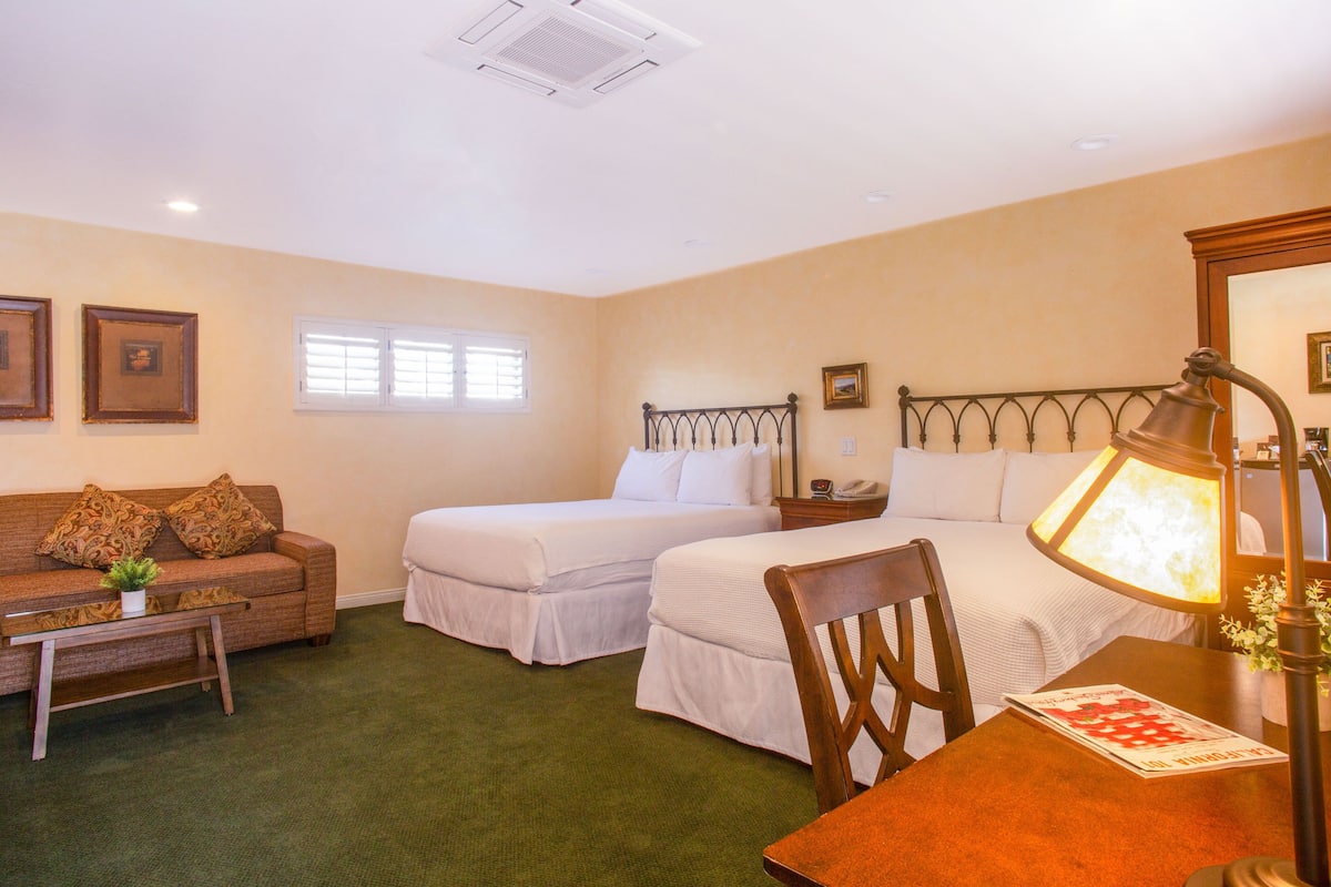 A hotel room with two beds, a sofa, a table, and a lamp.
