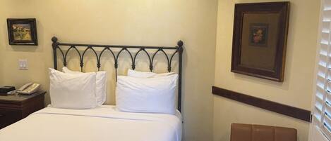 A hotel room with a bed, a chair, a nightstand with a phone, and two wall-mounted pictures.