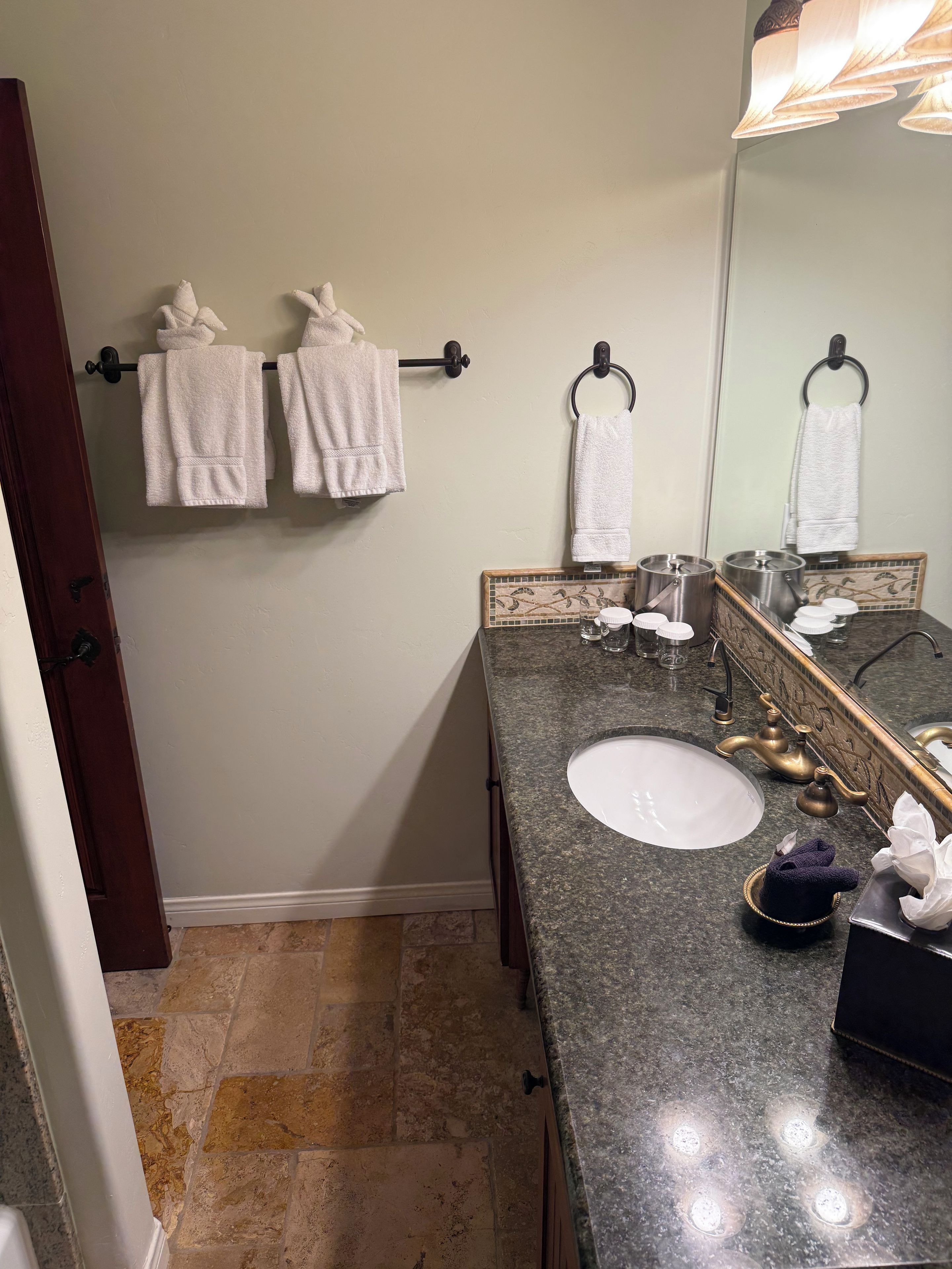 Une salle de bain avec un comptoir en granit, un lavabo blanc, un miroir et deux porte-serviettes avec des serviettes blanches.